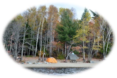 Attean campsite near waterway, on the Moose River Bow Trip, with trees in Autumn foliage behind.