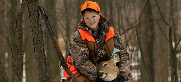 young female hunter in woods with deer and rifle