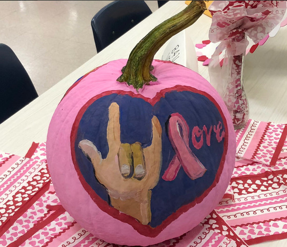 Pumpkin painted with a hand signing "love" and a ribbon 