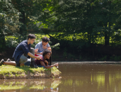 Students studying aquatic life while lying and kneeling near a riverbank